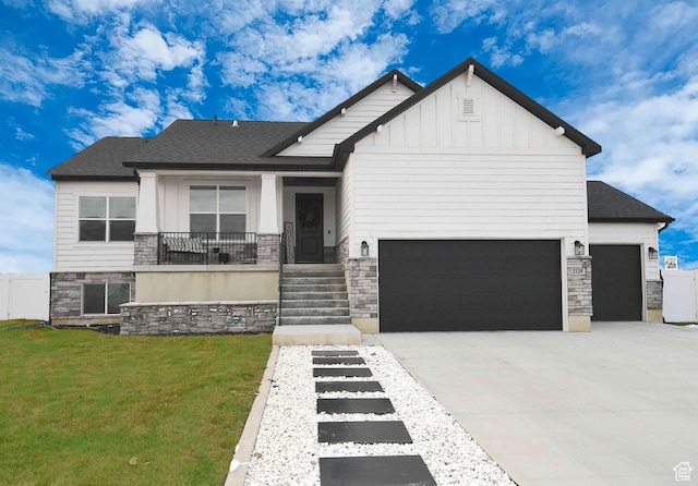 view of front facade featuring board and batten siding, a front yard, driveway, stone siding, and an attached garage