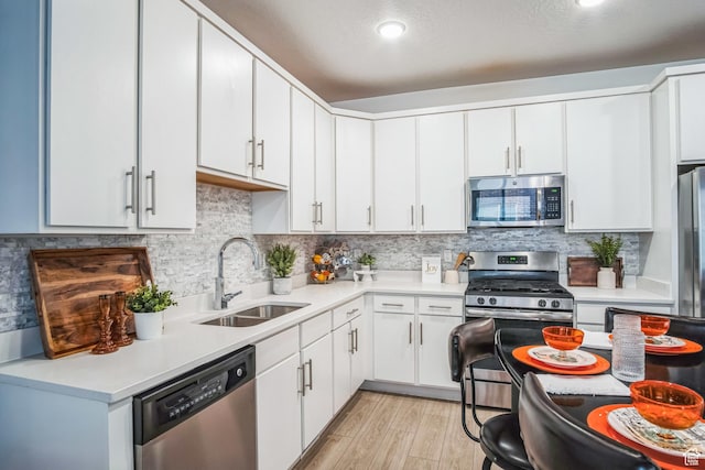 kitchen featuring decorative backsplash, light wood-type flooring, white cabinets, appliances with stainless steel finishes, and sink