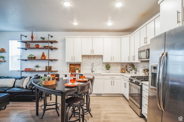 kitchen with appliances with stainless steel finishes, light wood-type flooring, sink, white cabinetry, and backsplash