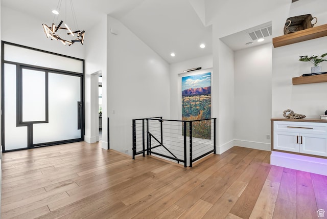 foyer featuring an inviting chandelier, high vaulted ceiling, and light wood-type flooring