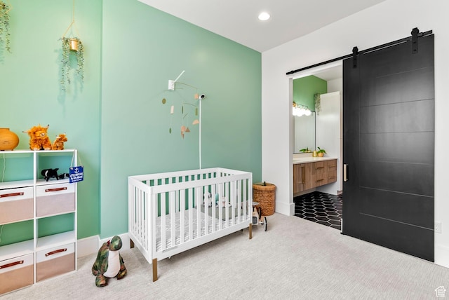 carpeted bedroom featuring a barn door, a crib, and ensuite bath