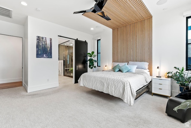 carpeted bedroom with connected bathroom, a barn door, ceiling fan, and wood walls