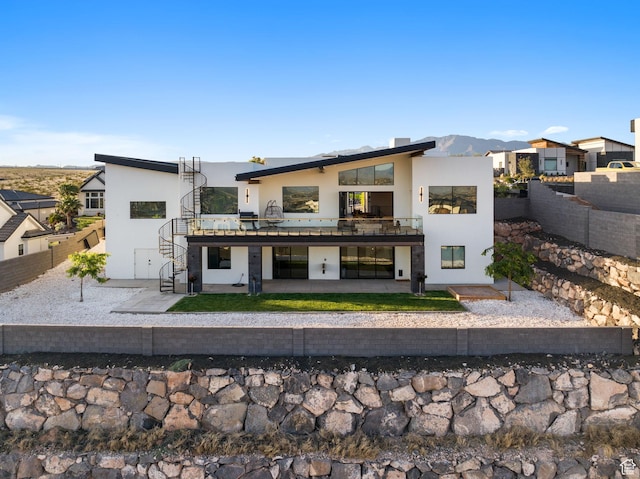 back of property with a mountain view, a balcony, and a patio area