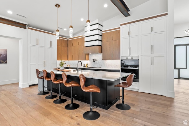 kitchen featuring decorative backsplash, pendant lighting, white cabinets, and an island with sink