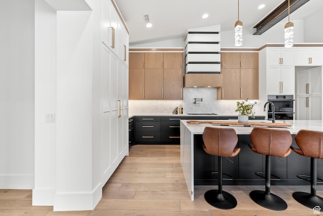 kitchen with vaulted ceiling with beams, decorative light fixtures, light hardwood / wood-style flooring, white cabinets, and a center island