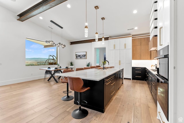 kitchen featuring light stone counters, an island with sink, decorative light fixtures, white cabinets, and light wood-type flooring