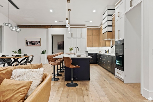 kitchen featuring white cabinetry, hanging light fixtures, light hardwood / wood-style flooring, a breakfast bar area, and a center island with sink