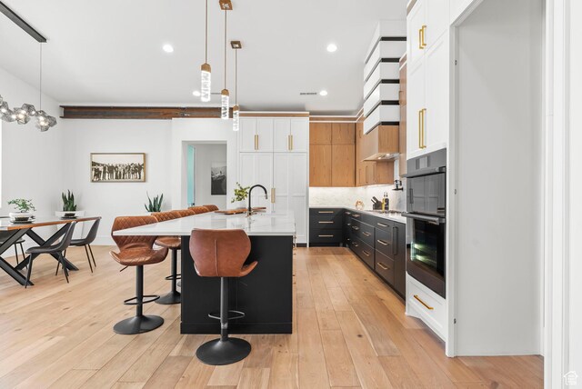 kitchen with pendant lighting, white cabinets, a kitchen bar, and a kitchen island with sink