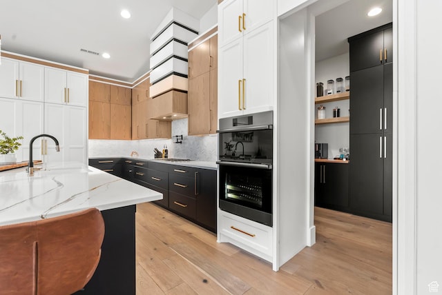 kitchen featuring double oven, light stone countertops, white cabinets, and light hardwood / wood-style floors