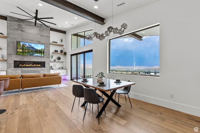 dining room featuring a tiled fireplace, ceiling fan, light hardwood / wood-style flooring, and beamed ceiling
