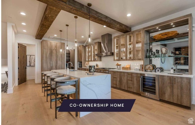 kitchen featuring pendant lighting, beamed ceiling, beverage cooler, and wall chimney range hood