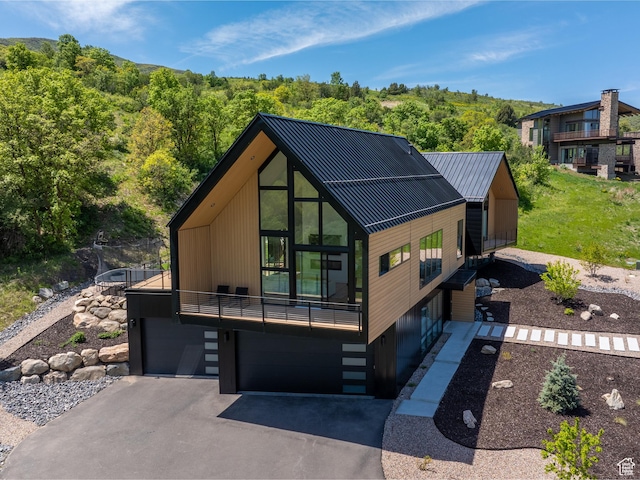 1113 S Quail Holw E, Huntsville, UT 84317 - modern home with a garage, a balcony, asphalt driveway, metal roof, and a view of trees