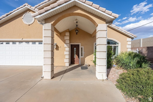 entrance to property featuring a tile roof, concrete driveway, fence, a garage, and stucco siding