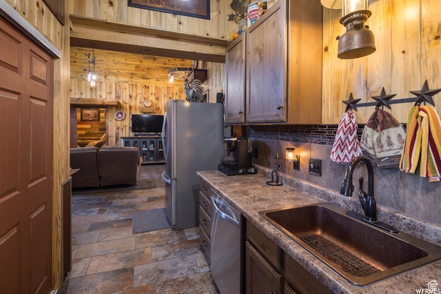 kitchen featuring appliances with stainless steel finishes, decorative light fixtures, wooden walls, and sink