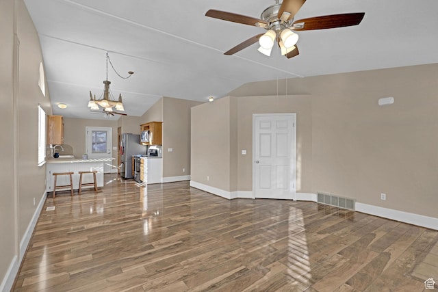 unfurnished living room with vaulted ceiling, dark wood-type flooring, and ceiling fan with notable chandelier