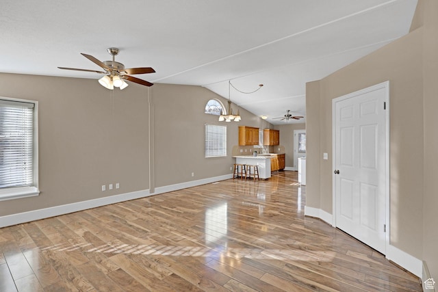 unfurnished living room featuring ceiling fan with notable chandelier, light wood-type flooring, and vaulted ceiling