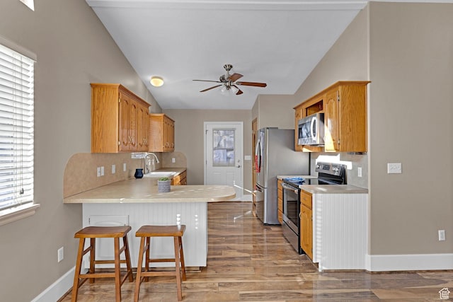 kitchen with sink, stainless steel appliances, vaulted ceiling, a kitchen bar, and light wood-type flooring