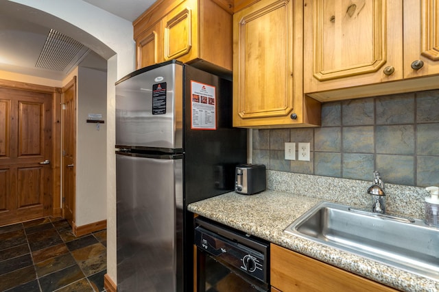 kitchen with dishwasher, backsplash, sink, stainless steel fridge, and light stone countertops