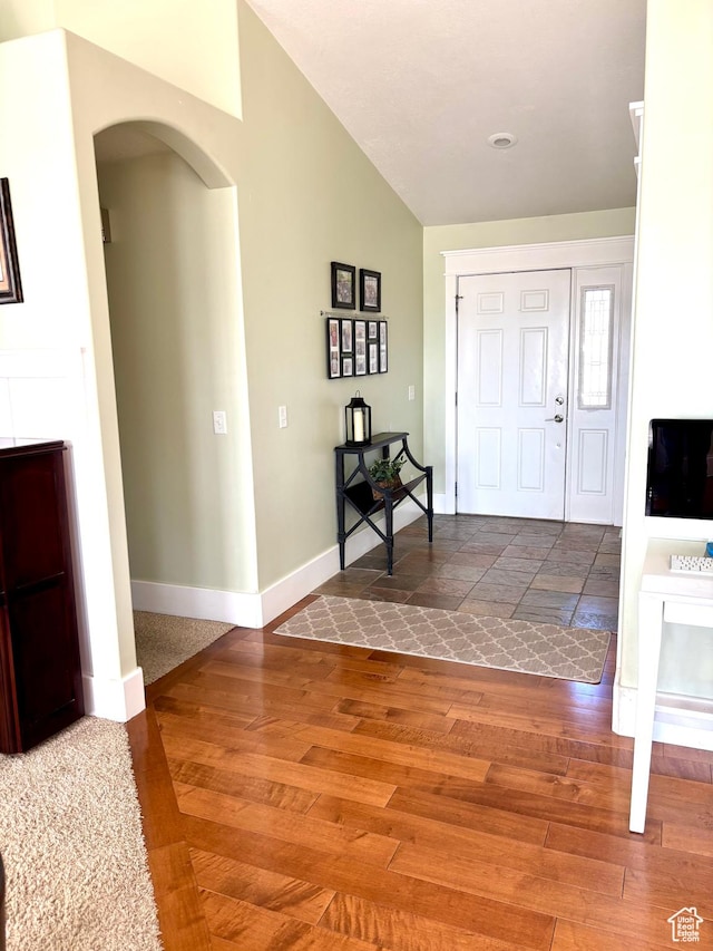 entrance foyer featuring arched walkways, wood finished floors, baseboards, and lofted ceiling