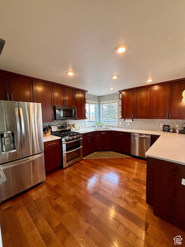 kitchen with appliances with stainless steel finishes, dark wood-type flooring, light countertops, decorative backsplash, and a sink