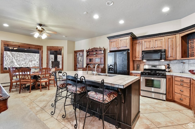 kitchen featuring a kitchen bar, sink, black appliances, tile countertops, and an island with sink