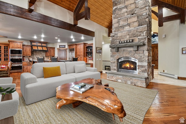living room featuring a stone fireplace, beamed ceiling, high vaulted ceiling, a baseboard heating unit, and light hardwood / wood-style floors