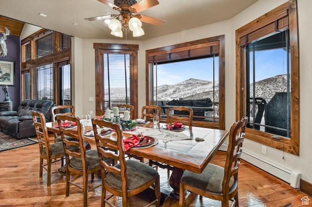 dining area with a mountain view, a healthy amount of sunlight, light hardwood / wood-style floors, and ceiling fan