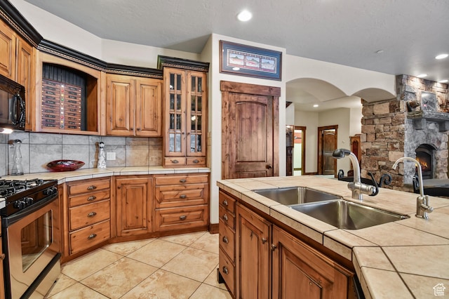 kitchen with tile countertops, a fireplace, stainless steel gas range oven, and sink