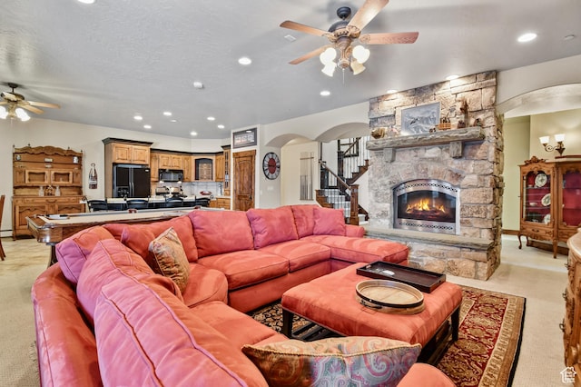 carpeted living room featuring a textured ceiling, a stone fireplace, and ceiling fan