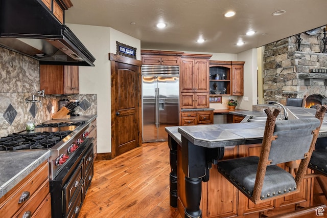 kitchen with light wood-type flooring, backsplash, stainless steel built in refrigerator, sink, and a breakfast bar area