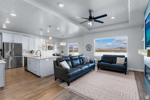 2217 E Emerald Ave, Eagle Mountain, UT 84005 - living room featuring a textured ceiling, light wood-style flooring, a glass covered fireplace, ceiling fan, and baseboards