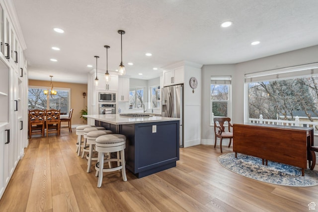 kitchen featuring stainless steel appliances, white cabinets, light hardwood / wood-style floors, a kitchen island, and pendant lighting