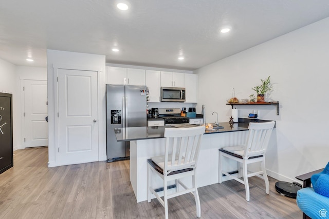 kitchen with kitchen peninsula, light hardwood / wood-style flooring, appliances with stainless steel finishes, a kitchen bar, and white cabinetry