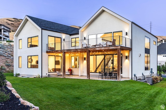 rear view of property with a balcony, a patio area, and a lawn