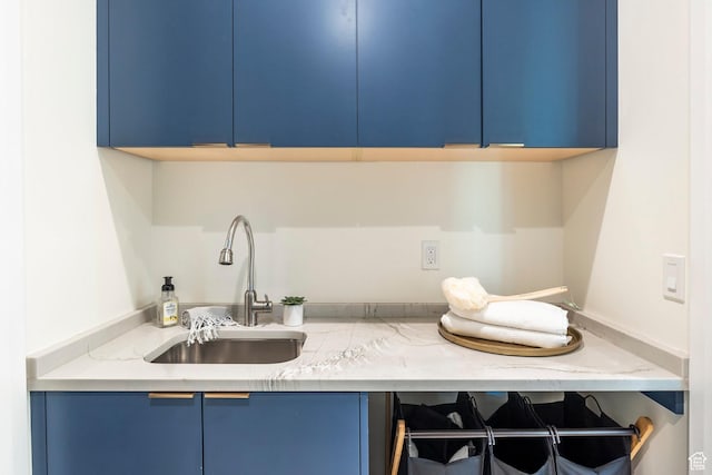 kitchen featuring light stone counters, blue cabinets, and sink