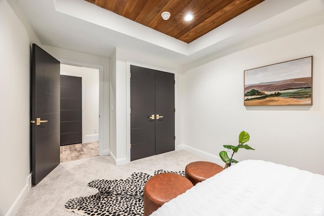 carpeted bedroom with a tray ceiling, a closet, and wood ceiling