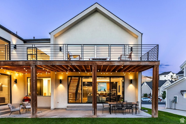 back house at dusk featuring a patio area and a balcony