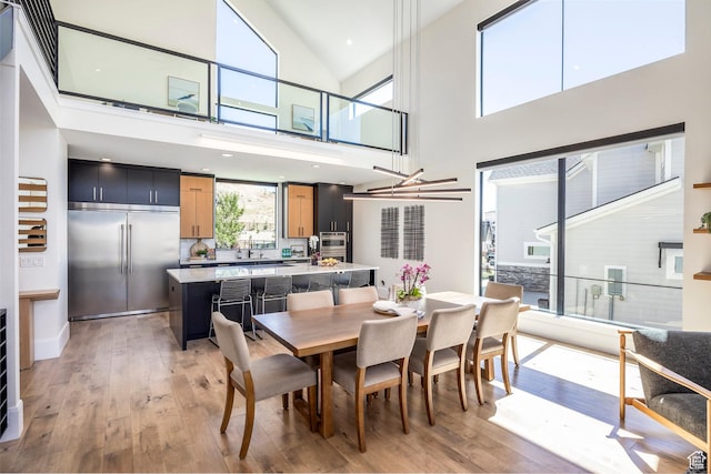 dining area featuring a high ceiling, light hardwood / wood-style floors, and an inviting chandelier