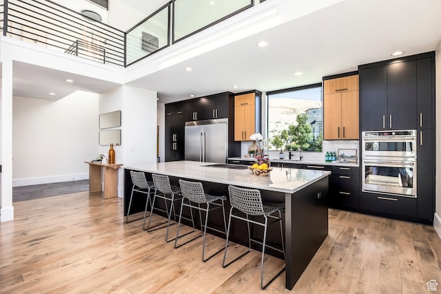 kitchen with light stone countertops, appliances with stainless steel finishes, light wood-type flooring, a kitchen breakfast bar, and a center island