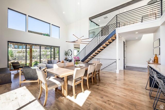 dining space with hardwood / wood-style floors, a towering ceiling, and an inviting chandelier