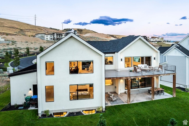 back house at dusk featuring a balcony, a yard, and a patio