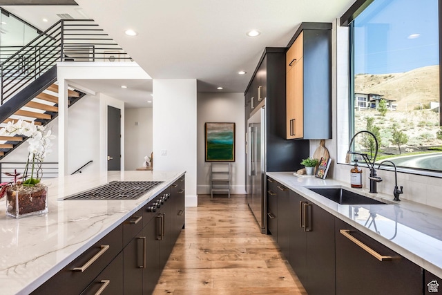 kitchen with high end refrigerator, light wood-type flooring, light stone counters, sink, and a mountain view