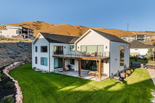 rear view of property featuring a lawn, a mountain view, a balcony, and a patio