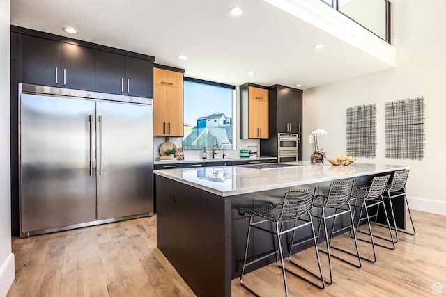 kitchen featuring built in fridge, light stone countertops, light wood-type flooring, a kitchen island, and a kitchen bar