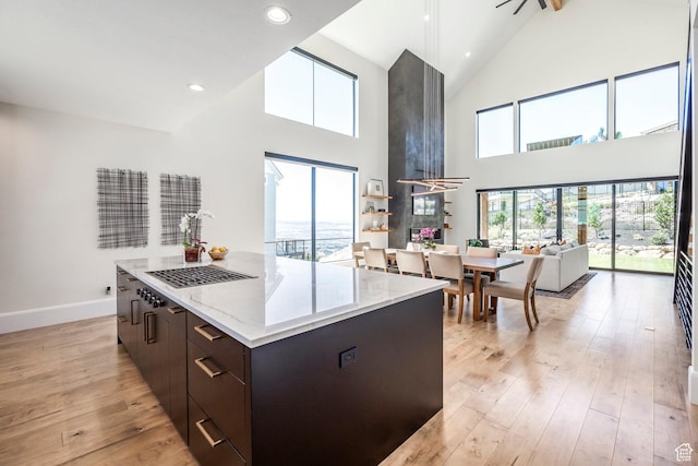 kitchen with dark brown cabinets, light wood-type flooring, a kitchen island, and a high ceiling
