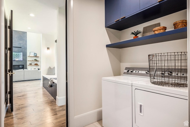clothes washing area featuring washer and clothes dryer, cabinets, and light wood-type flooring