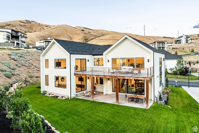 rear view of property featuring a balcony, central air condition unit, a patio area, a mountain view, and a yard