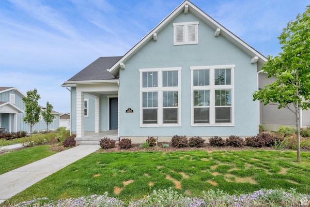 bungalow-style house featuring covered porch, a front yard, stucco siding, and a shingled roof