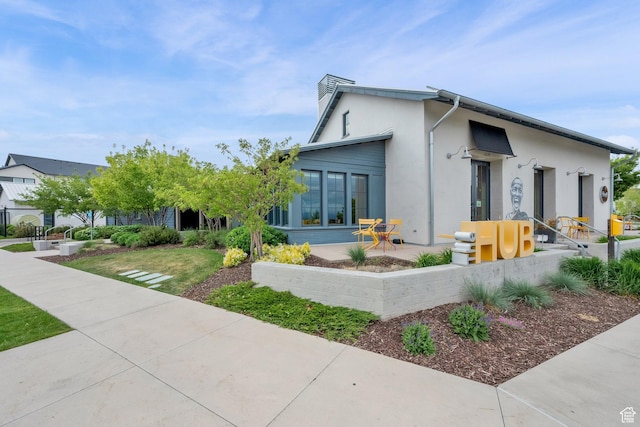 view of front of house with stucco siding, a chimney, and a patio area