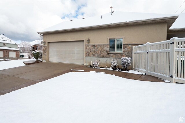 4876 S 1525 E, Ogden, UT 84403 - view of snow covered exterior with an attached garage, fence, stucco siding, stone siding, and driveway